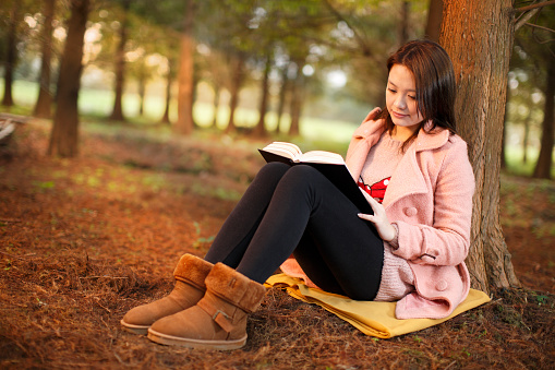 Asian woman relying on the tree and reading a book and enjoy the quiet ; shot with very shallow depth of field