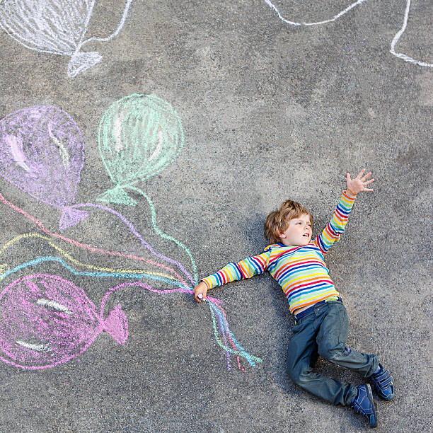 istock Kid boy having fun with colorful balloons drawing with chalks 501394262