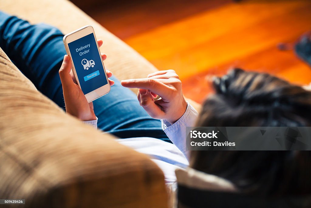 Woman using on line tracking in a mobile phone. Delivery order message in a mobile screen. Woman reading it at home. Pursuit - Concept Stock Photo