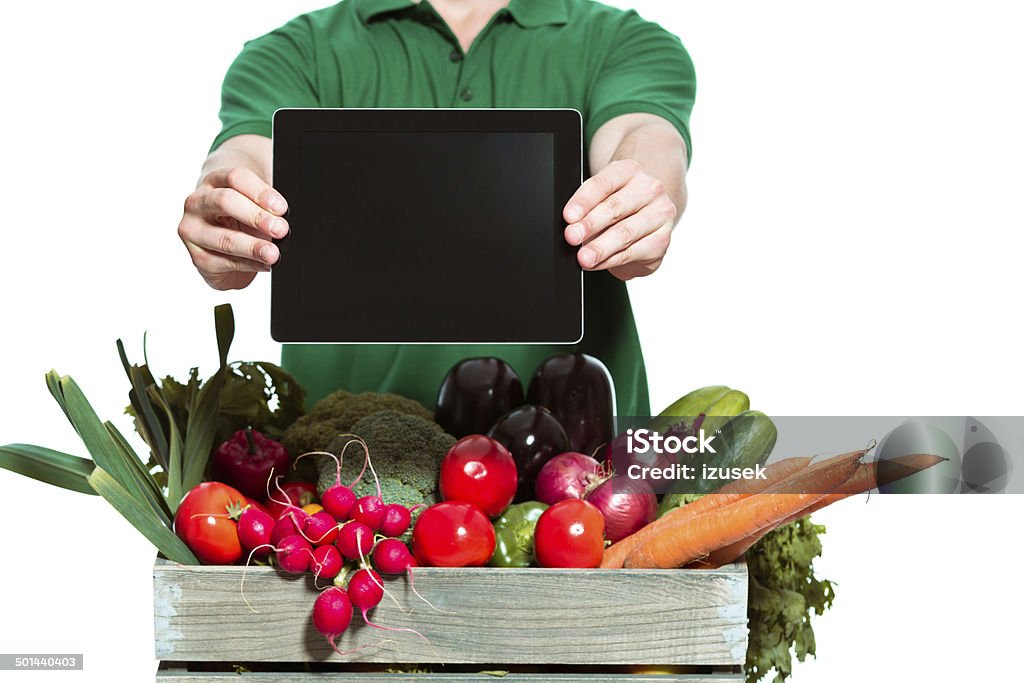 Delivery man with digital tablet Delivery man delivering box with organic food, holding digital tablet in hands. Close up of digital tablet. Studio shot, white background. Adult Stock Photo Delivery man with digital tablet Delivery man delivering box with organic food, holding digital tablet in hands. Close up of digital tablet. Studio shot, white background. Adult Stock Photo
