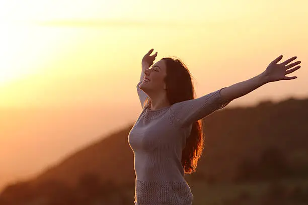 Photo of Woman at sunset breathing fresh air raising arms