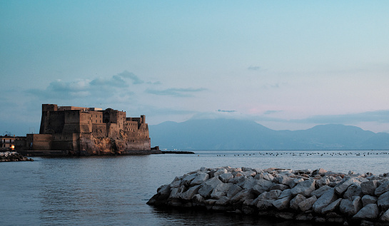 Napoli, Italy - December 12, 2015: Castel dell'Ovo is widely used in graphical memes to symbolise the city of Naples. In this photo, this ancient castle is seen from the seafront (via Partenope). The mount Vesuvius (Vesuvio), with its volcano, is visible in the background.