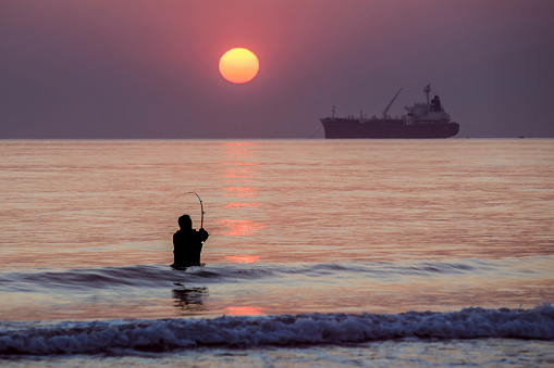 Fisherman fishes on the sea. Silhouette at sunset