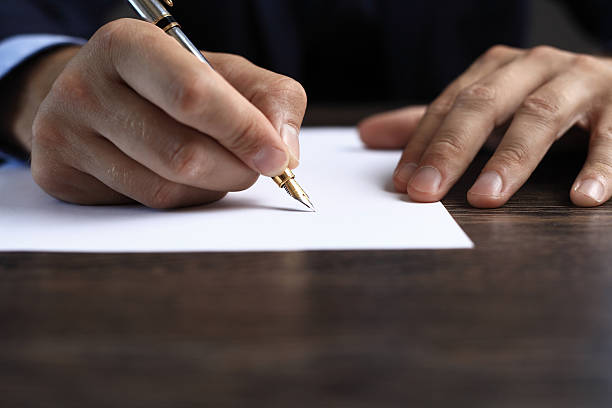 Man signing a document or writing correspondence Man signing a document or writing correspondence with a close up view of his hand with the pen and sheet of notepaper on a desk top. editor page stock pictures, royalty-free photos & images
