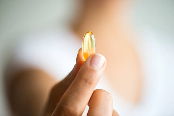 mujer agarrando y mostrando omega 3 cápsulas - fish oil vitamin e cod liver oil nutritional supplement fotografías e imágenes de stock