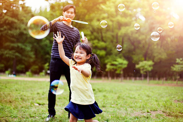 père et fille s'amuser dans le parc avec des bulles de savon - bubble child bubble wand blowing photos et images de collection