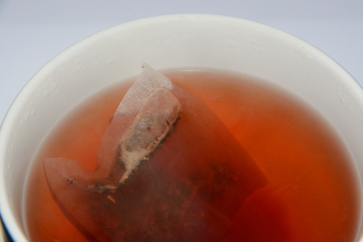 Steeping raspberry herbal tea with teabag in coffee cup and water droplets from heat and condensation on cup edge
