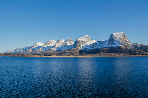 A whole Seven sisters mountain range in late winter time with still some snow on the top. Blue sea and sky of cold northern Norway.