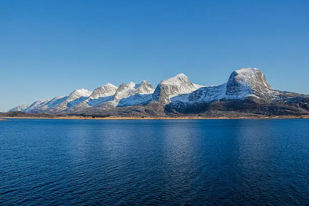 A whole Seven sisters mountain range in late winter time with still some snow on the top. Blue sea and sky of cold northern Norway.
