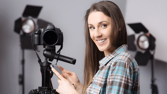 Young female photographer posing with a digital camera on tripod and lighting equipment on background