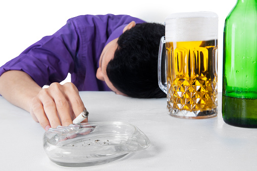 Drunk man sleeping on the table while holding cigarette, with a glass and bottle of beer
