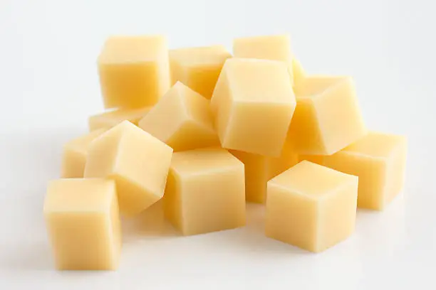 Photo of Cubes of yellow cheese stacked randomly on white.