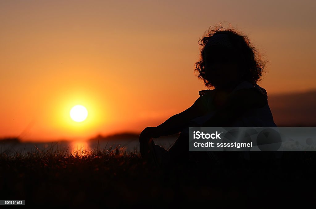 Relaxing young child in sunset Silhouette photo of relaxing young child at the lake in sunset Adult Stock Photo