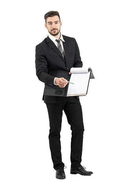 Young salesman in suit pointing signature space with pencil offering contract. Full body length portrait isolated over white studio background