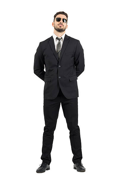 Secret agent or guard with hands behind back wearing sunglasses Secret agent or guard with hands behind back wearing sunglasses.Full body length portrait isolated over white studio background bodyguard full stock pictures, royalty-free photos & images