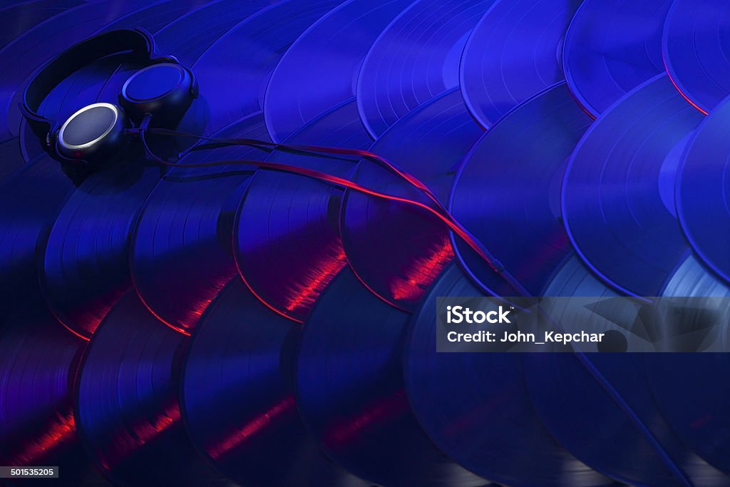 Colorful Array of Vinyl Records with Headphones A pair of headphones sitting on several vinyl records overlapping in an organized array and lit with red, blue, purple and white lights. Collection Stock Photo