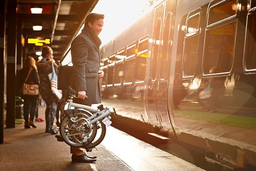 Businessman holding folding bicycle on railway platform about to board a train