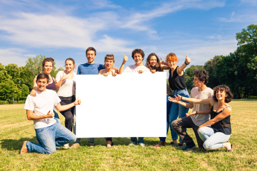 Ten Friends in a sunny day at the park holding a billboard for copy space.