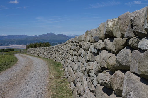 Typical Welsh stone wall on country track with Portmadog and Snowdonia mountains across the estuary.
