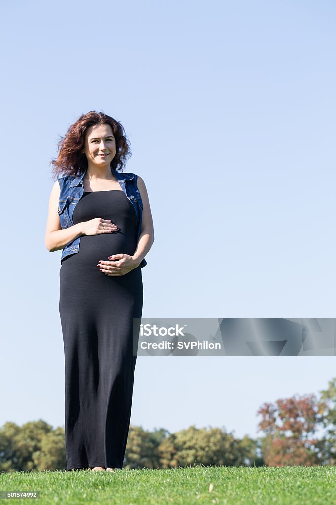 Pregnant woman is standing on the green lawn. Pregnant woman is standing on the green lawn. She is enjoying walk in the park. 2015 Stock Photo