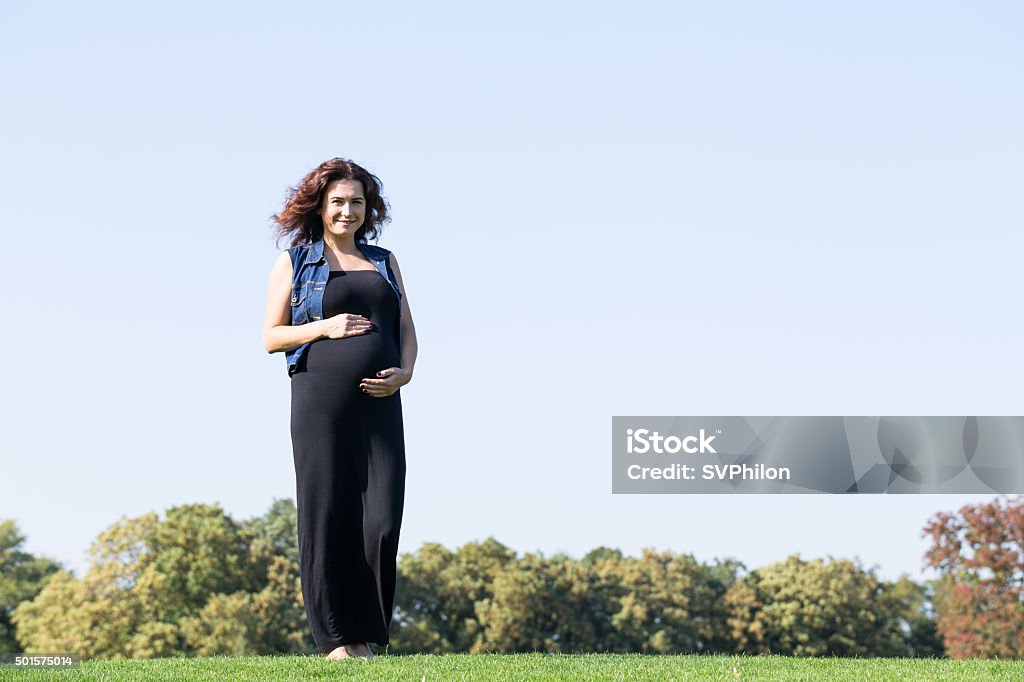 Pregnant woman is standing on the green lawn. Pregnant woman is standing on the green lawn. She is enjoying walk in the park. 2015 Stock Photo