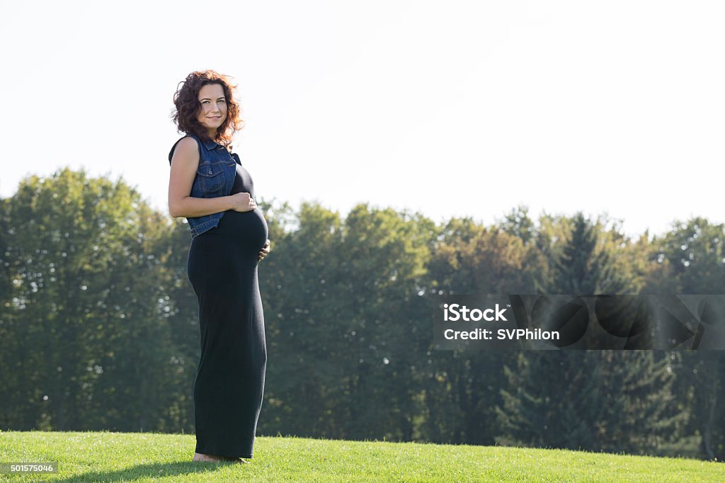 Pregnant woman is standing on the green lawn. Pregnant woman is standing on the green lawn. She is enjoying walk in the park. 2015 Stock Photo