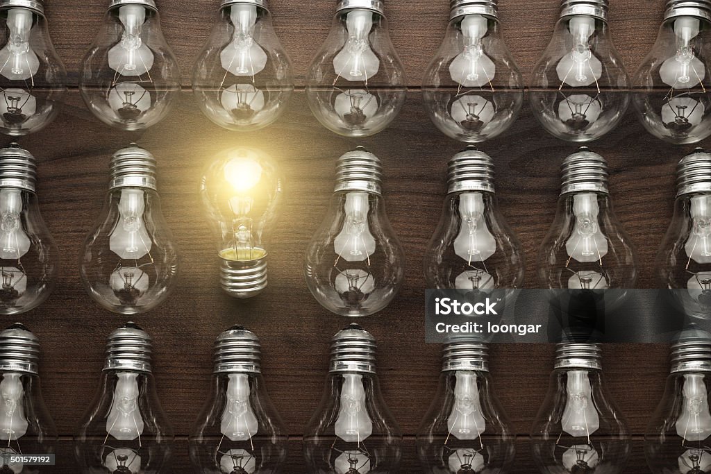 glowing bulb uniqueness concept glowing bulb uniqueness concept on brown wooden table Discovery Stock Photo