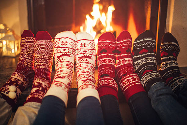 Füße in Weihnachtssocken in der Nähe des Kamins.  Vier Paar Füße beim Aufwärmen. Freunde im gemütlichen Winterurlaub.