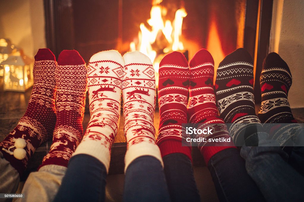 Friends at cozy winter vacation. Feet in Christmas socks near fireplace.  Four pair of feet warming up. Friends at cozy winter vacation. Christmas Stock Photo