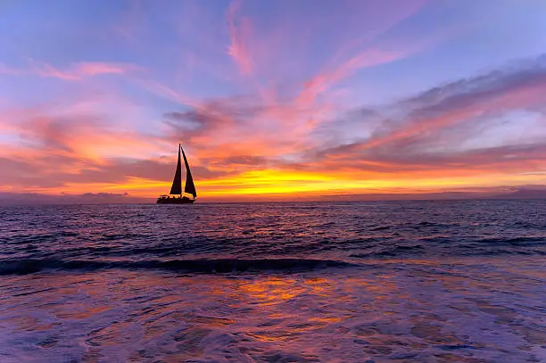 Sailboat sunset silhouette is a colorful vibrant orange and yellow cloudscape sunset.