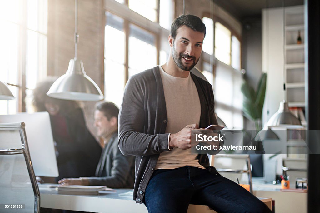 Homme d'affaires souriant avec téléphone portable assis dans son bureau - Photo de Hommes libre de droits