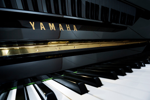 Milano, Italy - December 9, 2015: Keyboard of Yamaha vertical piano from very close, macro, point of view. The Yamaha brand name has light spot making it more vivid.  Very selective focus, tilt function of the camera lens allows  front to back depth of field particularly in the Yamaha brand name.  Mostly all the black keys are in focus leaving the white side of the keyboard with slightly out of focus effect. There are many diagonal in the picture each one created by the keyboard and other Parts of the Piano. On the upper side of the picture there are reflections of the keybord making the  picture quite intrigant. The complete image is in a low key profile. Landscape view, no people.