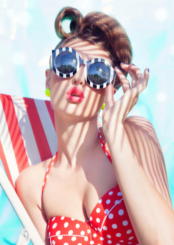 Colorful summer portrait of young attractive woman wearing bikini and sunglasses sitting by the swimming pool