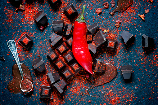Dark chocolate, red chili pepper, dry pepper on dark stone background, top view, selective focus
