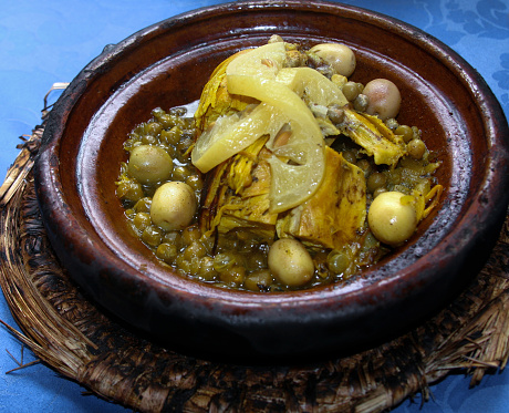 A chicken tagine with olives and lemon on an old charred plate and placemat. Shot in a traditional Morocco restaurant.