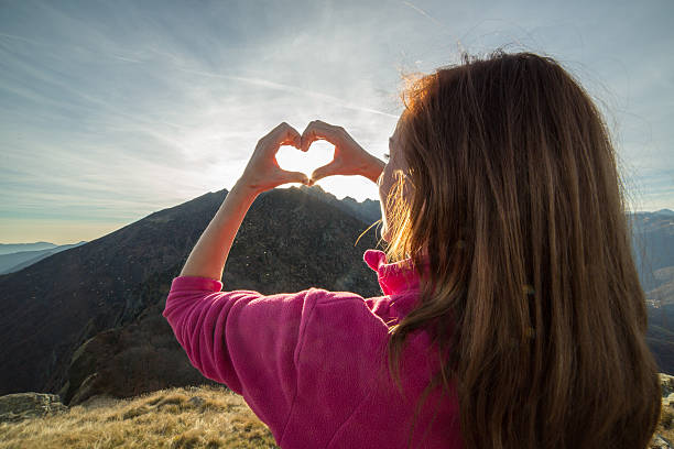 istock Young woman on mountain top makes heart shape finger frame 501618946