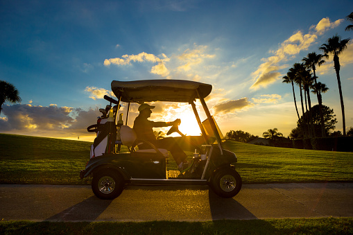 Senior man on golf course driving golf cart at sunrise