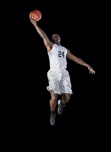 Athletic African american basketball player jumping high and scoring a layup. Shot on a Black Background
