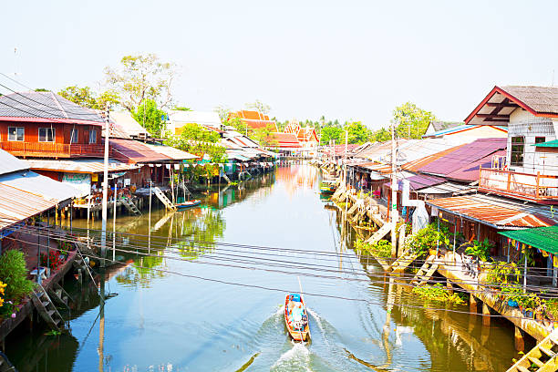 Amphawa, Thailand - March 13, 2014: Aerial shot from bridge of river and Thai senior man passing along river and old traditional wooden buildings at floating market in Amphawa. Daily scene during week, no market scene. Warm sunshine of afternoon over river and scenery. 