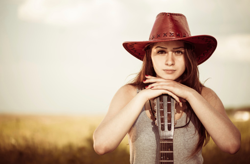 young pretty brunet woman in red hat and guitar at countryside meadow