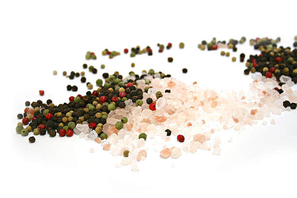 Scattered pile of Himalayan pink salt & mixed peppercorns, shallow depth of field on white background