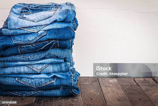 Stack Of Various Shades Of Blue Jeans On Old Wood Stock Photo - Download Image Now - Jeans, Denim, Fashion