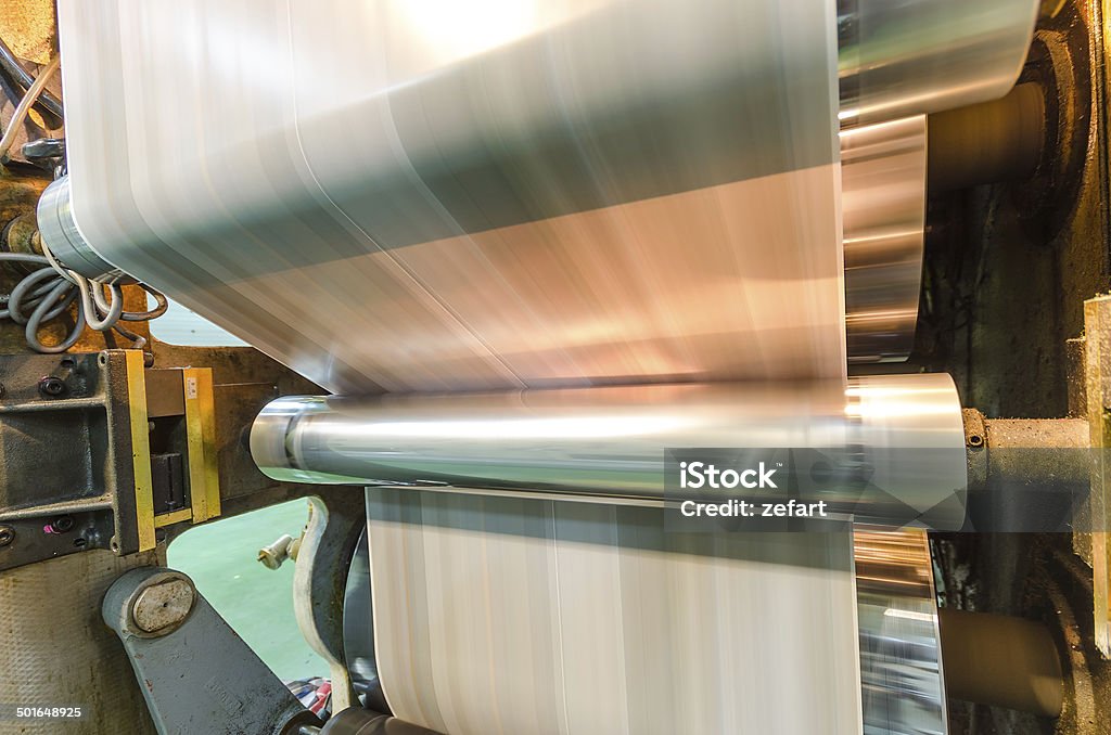 Large webset offset printing press running a long roll paper A large webset offset printing press running a long roll off paper over its rollers at high speed. Newspaper Stock Photo