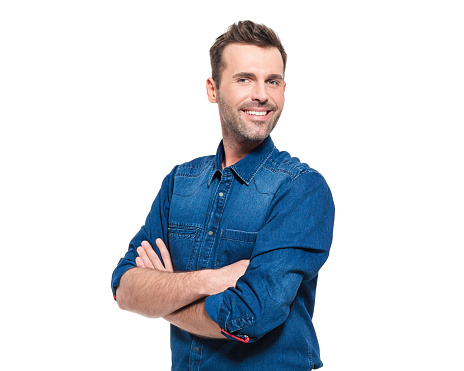 Portrait of happy adult man wearing jeans shirt, standing against the white background with arms crossed, smiling at camera.