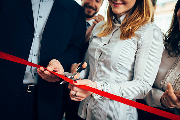 We will always remember this day! CEO and his assistant cutting a red ribbon, opening ceremony. Few people are in back and they are smiling. They are starting a new business. opening event stock pictures, royalty-free photos & images