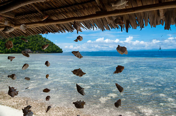 Shells hanging from bamboo roof in front of the blue ocean and white sand beach in Raja Ampat, Papua New Guinea, Indonesia