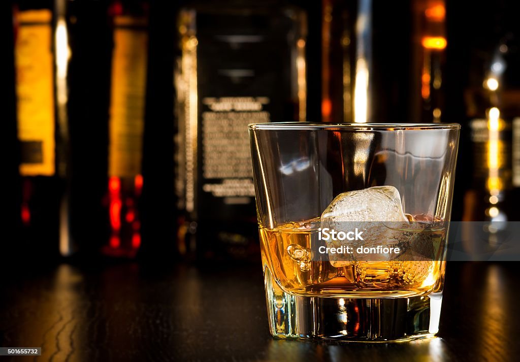 whiskey glass with ice in front of bottles whiskey glass with ice in front of bottles on wood table Bottle Stock Photo
