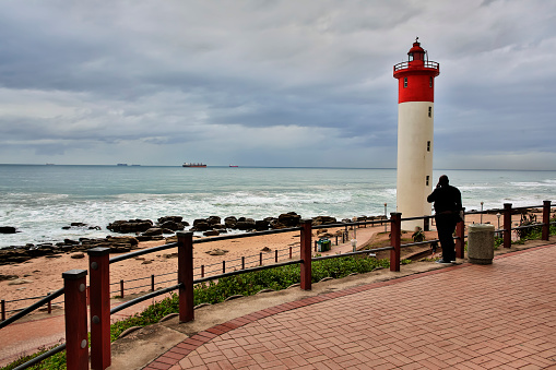 Durban, South Africa -July, 5th - 2014, Man speaks on cell phone looking out to container ships with Umhlanga Lighthouse on his right.