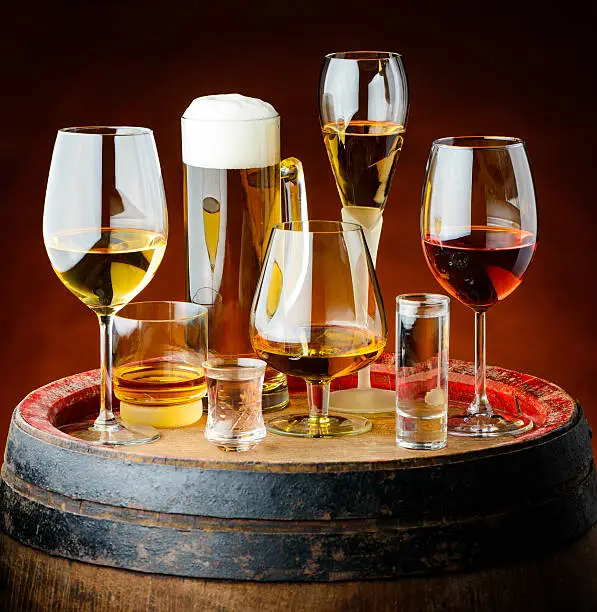 Alcoholic drinks in glasses on a wooden barrel in a cellar.