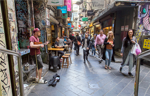 Melbourne, Australia: October 7, 2015: Street Busker playing a ukulele in a narrow street in Melbourne. Passing people are watching him. 
